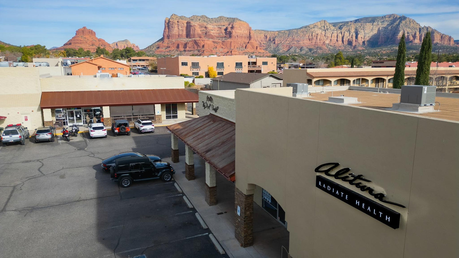 Commercial building with 'Alitura' sign, cars parked, and mountains in the background