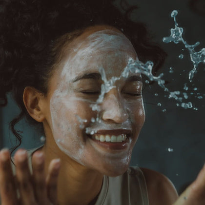 Photo of beautiful woman using Alitura Pearl Cleanser on her face and splashing water on her face