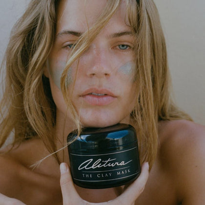 Photo of beautiful woman holding Alitura Clay Mask with it also applied on her cheeks