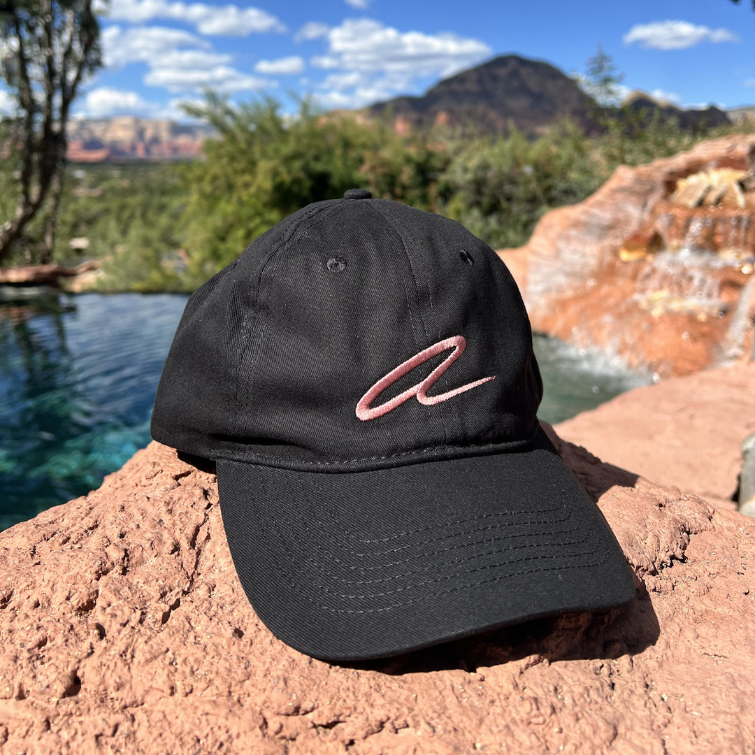 Black cap with pink Alitura logo on a rock with a scenic background
