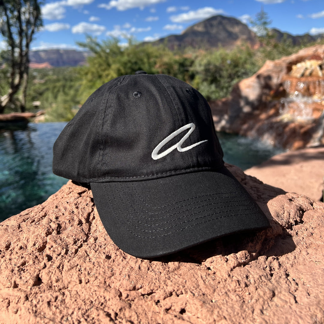 Black cap with a white Alitura logo on a rock with a scenic background