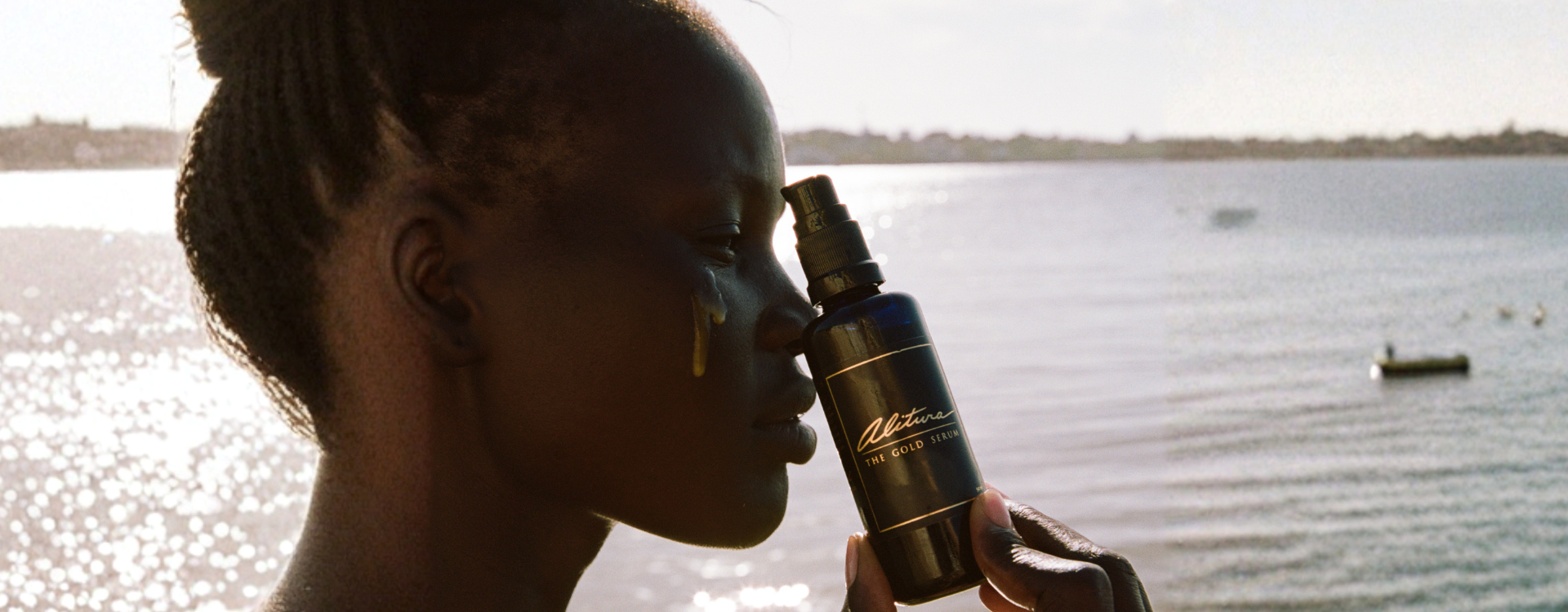 Woman holding and using Alitura Gold Serum next to body of water