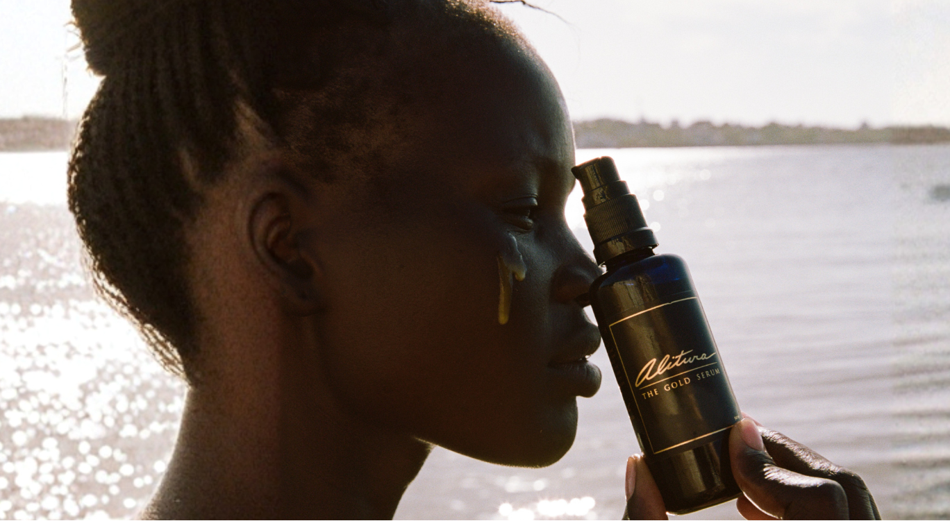 Woman holding and using Alitura Gold Serum next to body of water