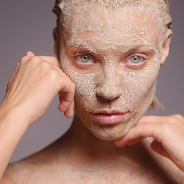 Woman applying a Alitura clay mask on a gray background